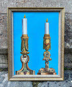 Decorative candlesticks in a gold frame against a blue background on a stone wall.